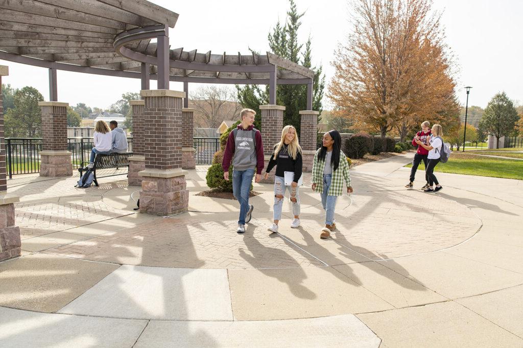 Three students walking across a round, paved area.